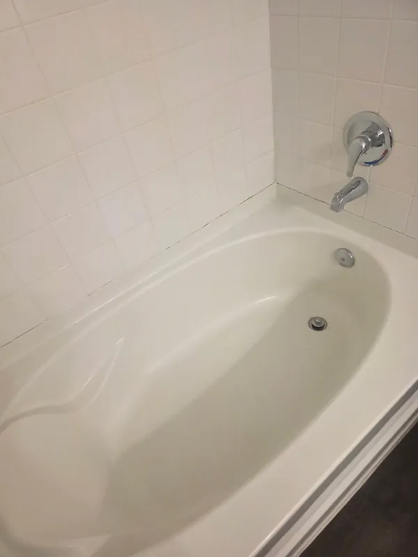 After: the same white bathtub from a similar angle, tub floor and walls bright and clean.
